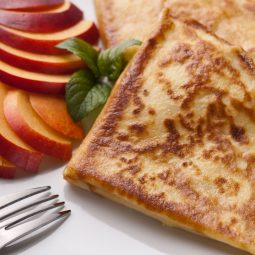 Wegetariańskie naleśniki z serem podane na białym talerzu razem z kawałkami jabłka.