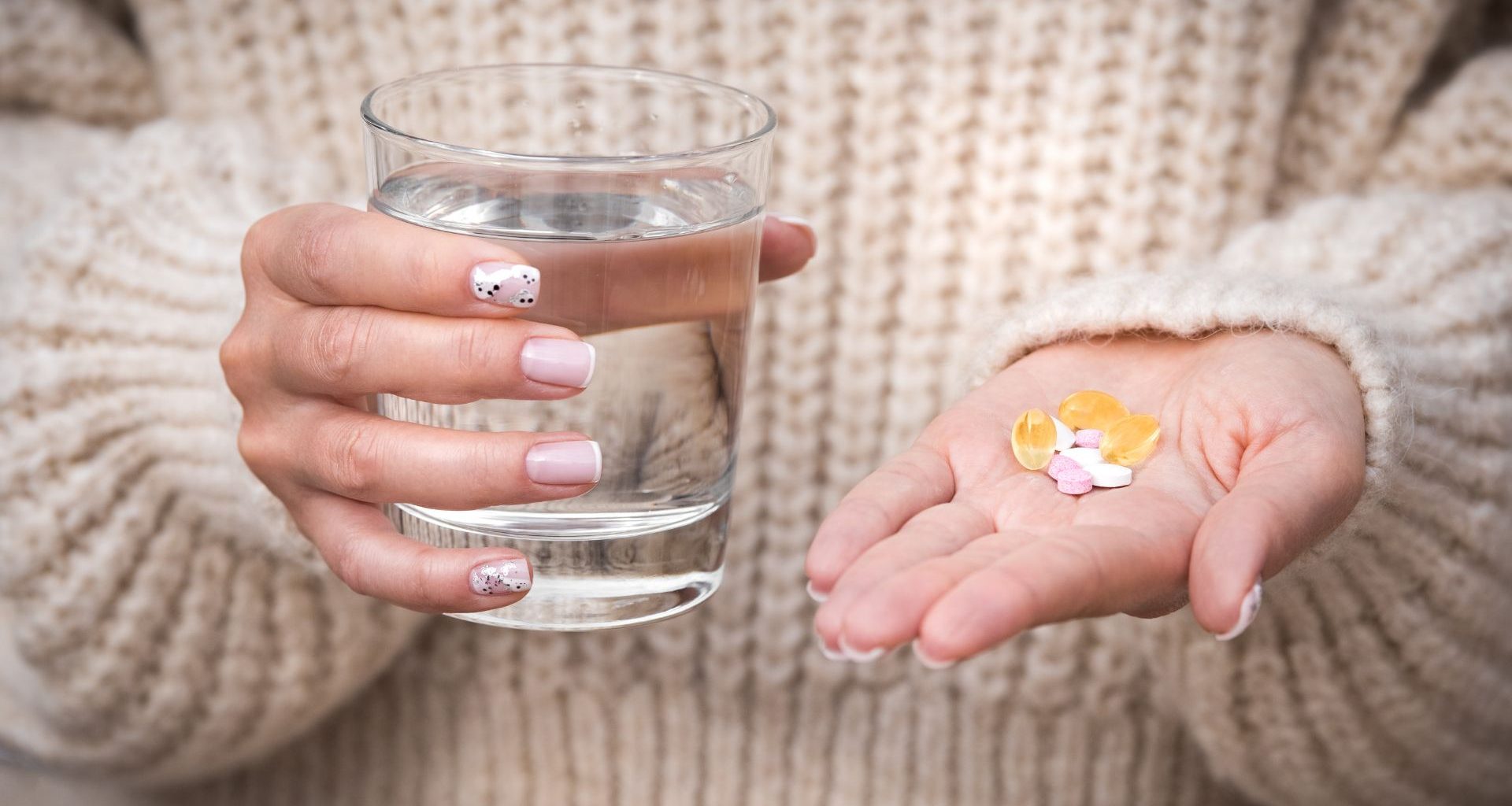 Kobieta trzyma szklankę z wodą w jednej i witaminy dla wegan w drugiej dłoni.