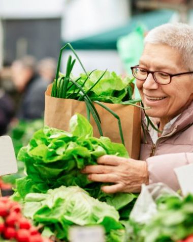Starsza kobieta wyznająca weganizm kupuje warzywa w sklepie.