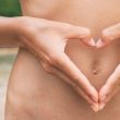Kiedy warto przyjmować probiotyki dla wegan? NA zdjęciu kobieta dłońmi pokazuje serca na brzuchu.