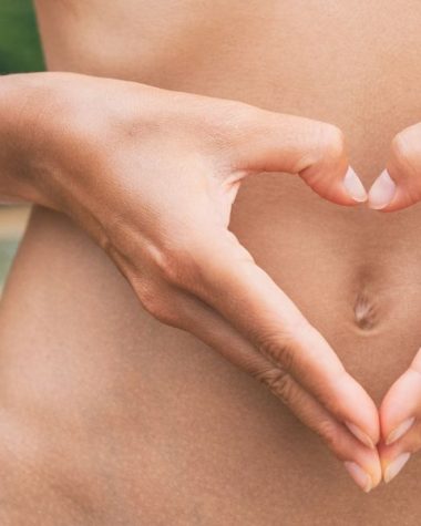 Kiedy warto przyjmować probiotyki dla wegan? NA zdjęciu kobieta dłońmi pokazuje serca na brzuchu.